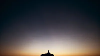 Silhouette of a person sitting alone on a bench at sunset