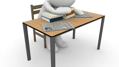 3D figure slumped over a desk with a pile of books, looking exhausted