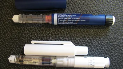 Two insulin pens with caps removed on a dark surface